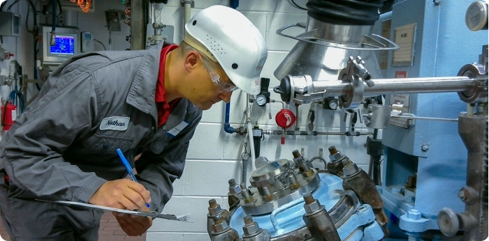 Technician inspecting pharmaceutical manufacturing equipment and recording data for quality control