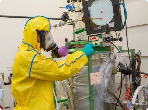 A Person in protective hazmat suit conducting hazardous chemical process safety testing in a pharmaceutical laboratory