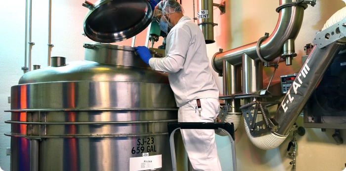 Technician operating stainless steel reactor in pharmaceutical manufacturing facility during drug production process