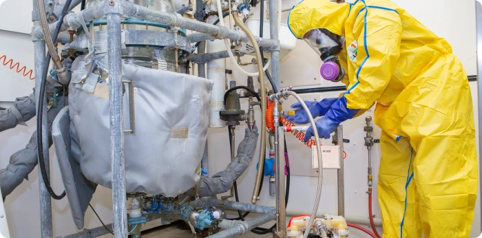 Technician in protective suit inspecting industrial reactor equipment in pharmaceutical API manufacturing facility
