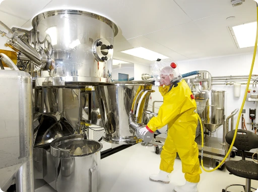 Worker in PPE managing high-potency API production system