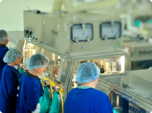 Pharma professionals in cleanroom uniforms working on sterile drug manufacturing equipment in GMP facility