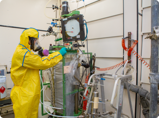 Technician in protective suit operating HPAPI pharmaceutical processing equipment in a contained manufacturing facility
