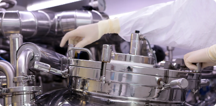 Cleanroom technician operating stainless steel pharmaceutical processing equipment for API manufacturing and drug production