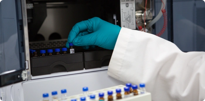 Scientist placing pharmaceutical sample vials into laboratory analytical testing equipment during drug research and quality control